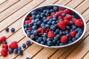 a bowl of blueberries and raspberries on a wood surface